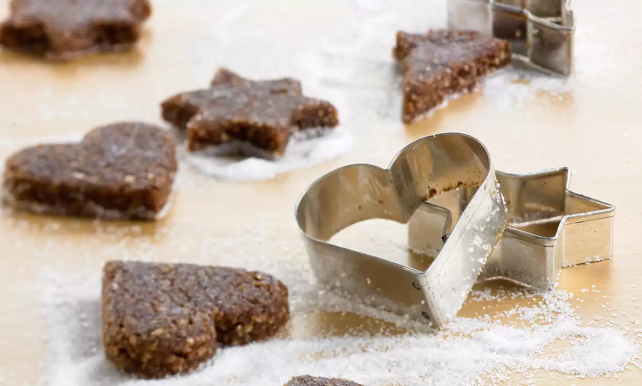 Biscuits bruns en forme de cœur et d’étoile à la texture granuleuse, saupoudrés de sucre glace sur une surface claire avec des emporte-pièces en métal
