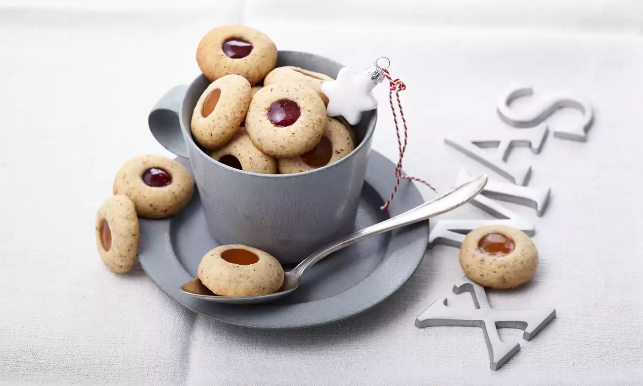 Prhki keksi svijetlosmeđe boje s glatkim punjenjem od marmelade i karamele smješteni u sivoj šoljici na platnenoj bijeloj podlozi