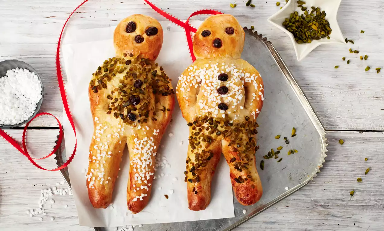 Hefeteig-Stutenkerl: goldbraune, frisch gebackene Männchen mit Rosinenaugen, Zuckerguss und leichtem Zuckerbelag auf Backpapier