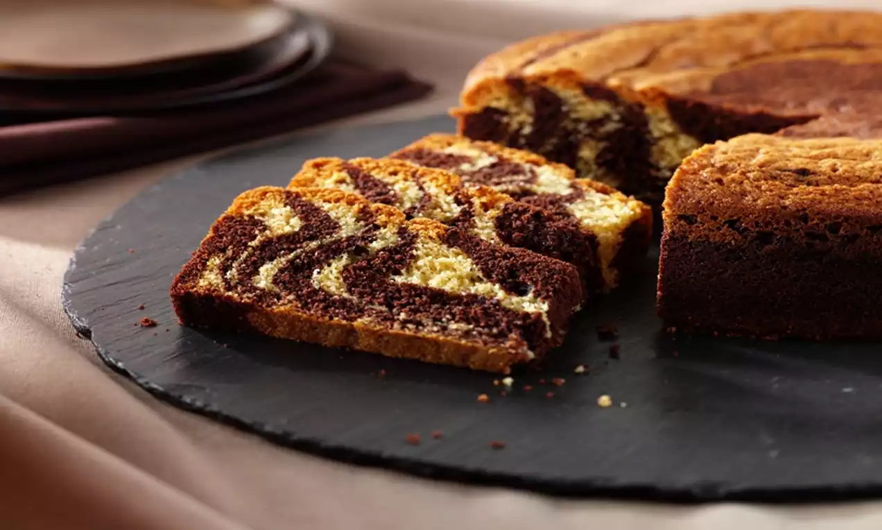 Zebra cake with marbled golden and dark brown stripes, soft texture, sliced and arranged on a round black slate plate