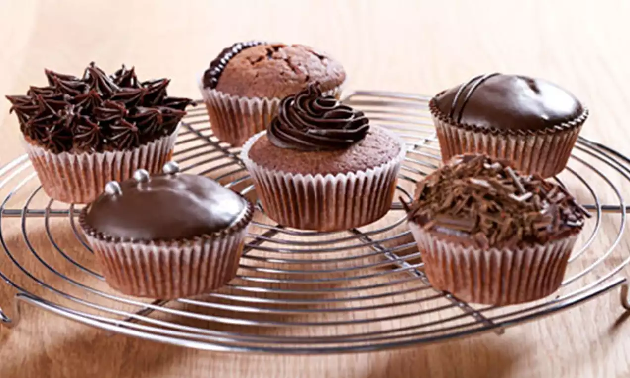 Zes chocoladecupcakes met glanzende glazuren, decoraties van room, parels en krullen, geplaatst op een metalen rooster op een houten tafel