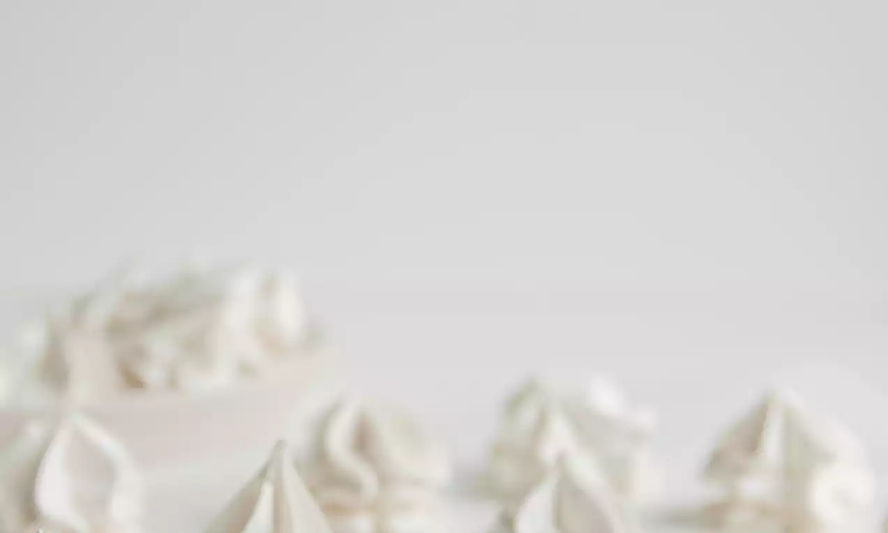 Rosaces de crème fouettée blanc neige aux courbes délicates, disposées sur une surface claire avec quelques éclats épars