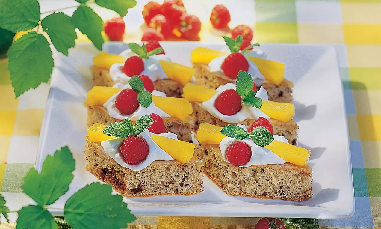 Auf einem weißen Teller liegen goldbraune Schnitten mit Sahnetupfen, gelben Mangostreifen, roten Himbeeren und frischen Minzblättern