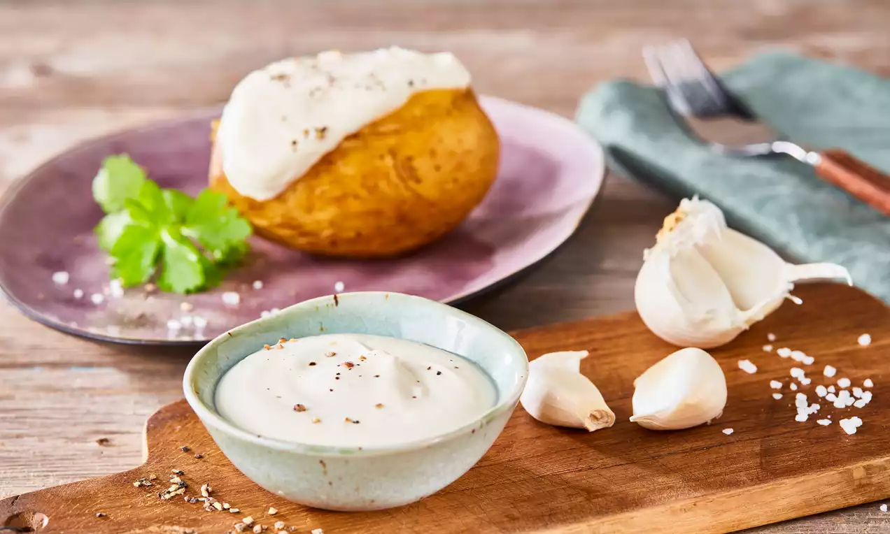 Sour Cream in einer kleinen weißen Schale, cremig weiß, bestreut mit fein gehacktem Schnittlauch, mit Löffel auf Holzbrett