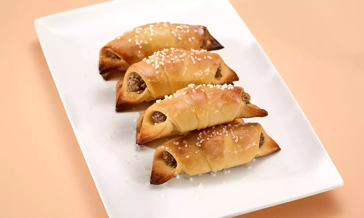 Piccoli cornetti dorati di pasta lievitata ripieni di noci tritate, disposti in fila su un piatto bianco e cosparsi di granella di zucchero