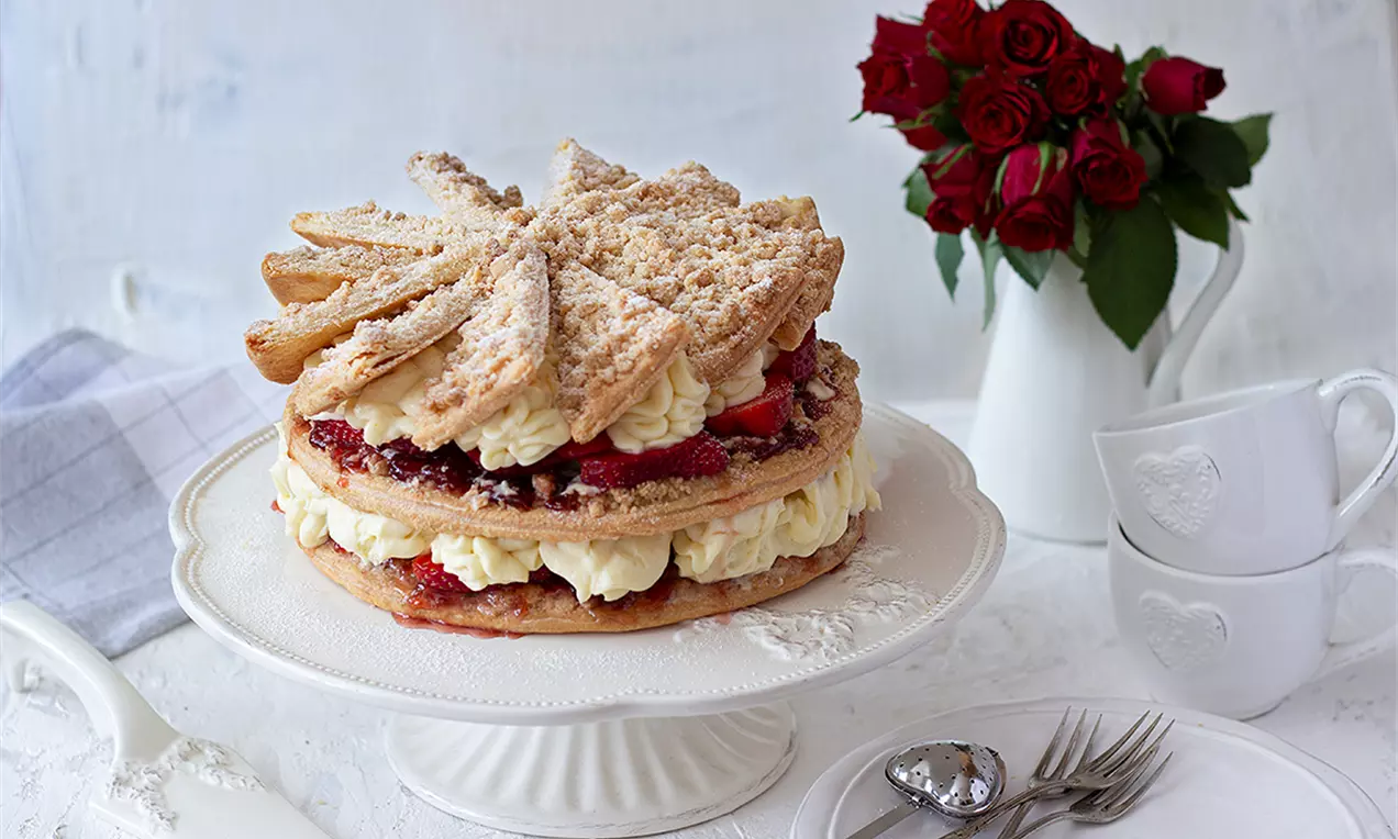 Кръгла немска торта с два пухкави слоени блата, между които има ванилов крем и сочни ягоди, украсена с захарен прах и поставена върху бяла стойка