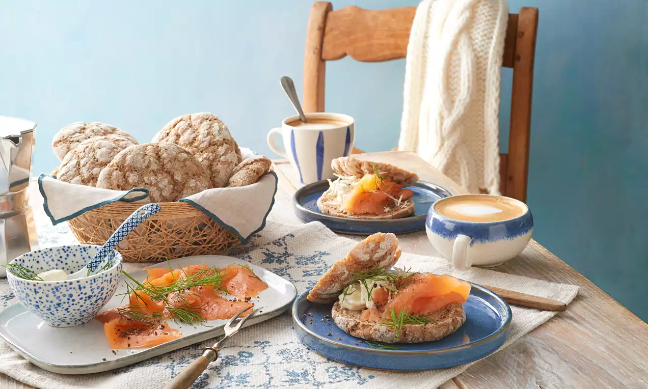 Ruisleipä: saftige finnische Roggenbrötchen mit dunkler Kruste, leicht bemehlt, auf Holzbrett neben Butter und Körnern