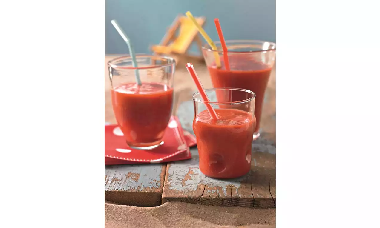 Smoothies d'un rouge rosé intense dans des verres transparents avec des pailles colorées, disposés sur une table en bois clair