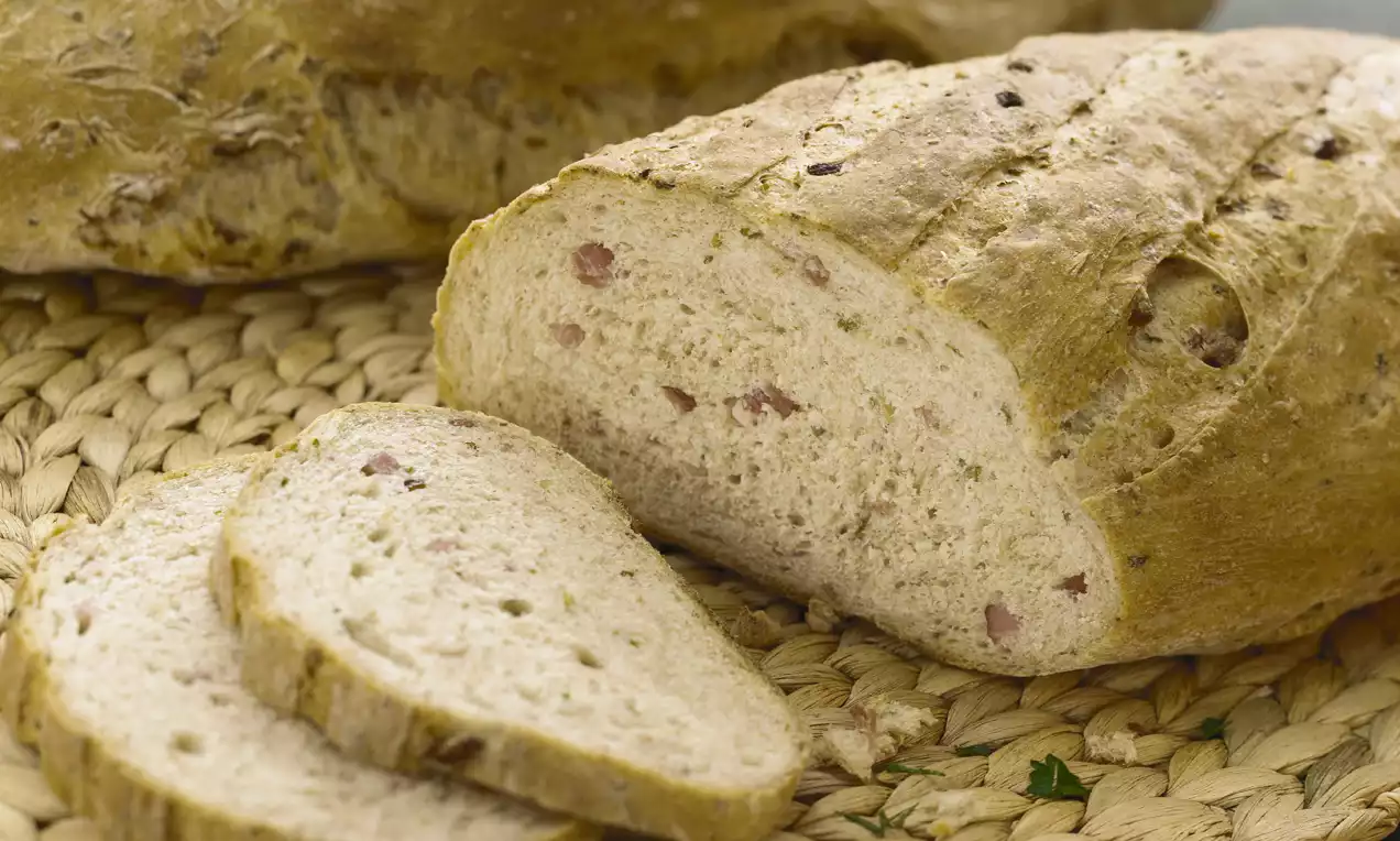 Lichtbruin spekbrood met knapperige korst, luchtig wit kruim met spekstukjes, deels in plakken gesneden op een rustieke placemat