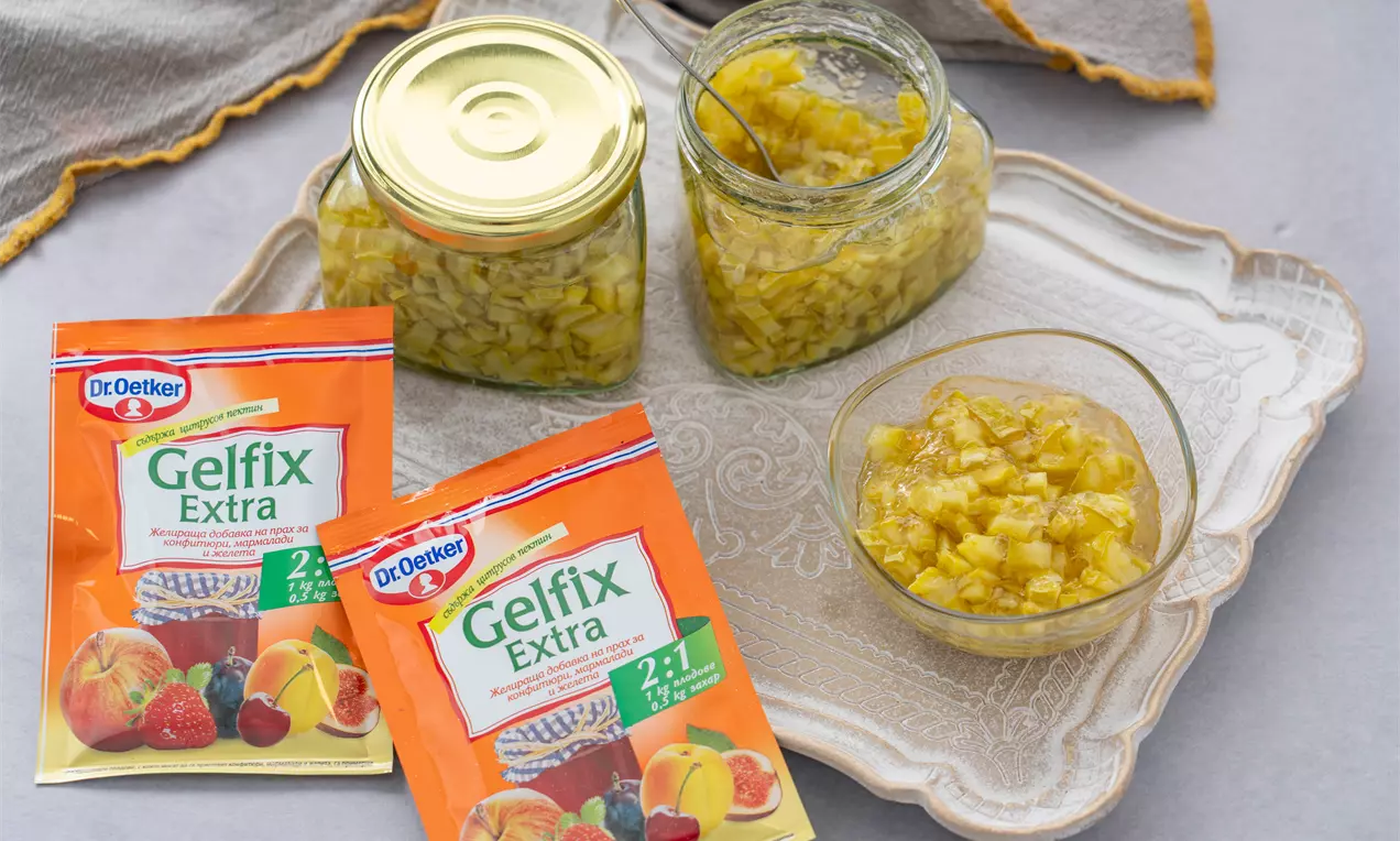 Златисто жълто сладко от тиквички с мека текстура в прозрачна купичка и стъклени буркани с капаци върху светла декоративна табла