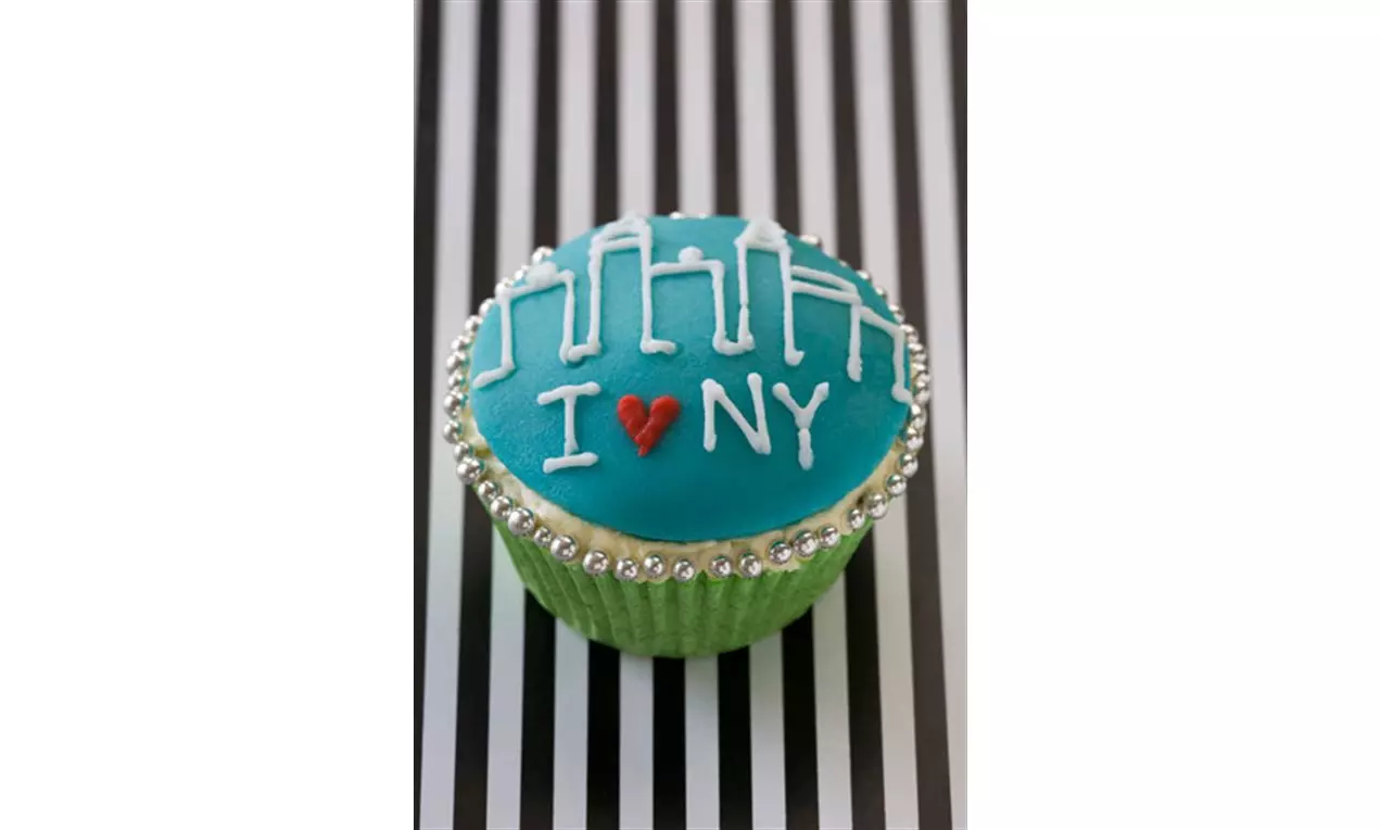 Cupcake med blå glasur dekorert med hvite bygninger, rødt hjerte og teksten "I ♥ NY", kantet med sølvpærler i grønt papirform