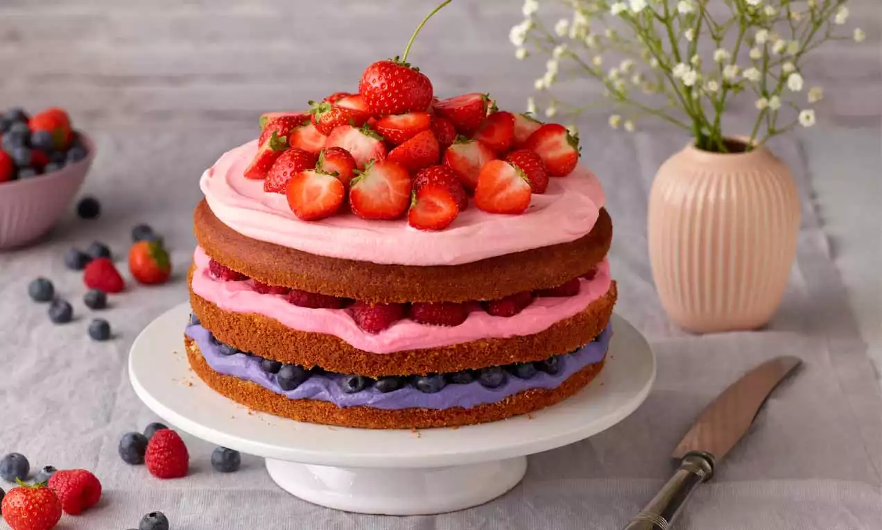 Ein Beeren-Naked-Cake mit drei Schichten hellbrauner Böden, gefüllt mit rosa und lilafarbenem Frosting, garniert mit frischen Erdbeeren