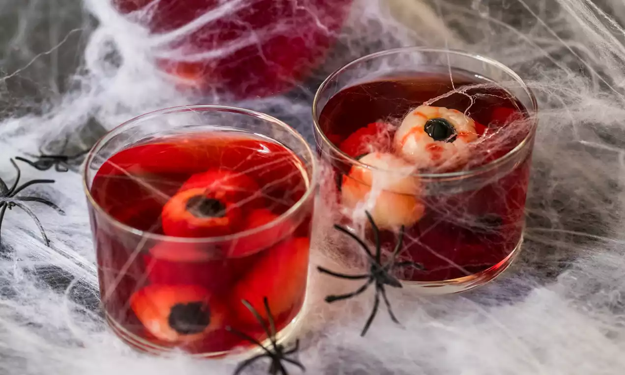 Mocktail de color rojo profundo en vasos bajos con ojos flotantes de gelatina blanca y negra rodeados de telarañas y pequeñas arañas negras
