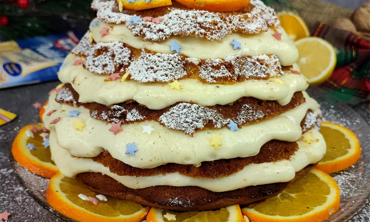 Торта “Пандоро” с пластове златисто тесто, крем и набраздени ръбове, поръсена с пудра захар, декорирана с резени портокал и захарни звезди