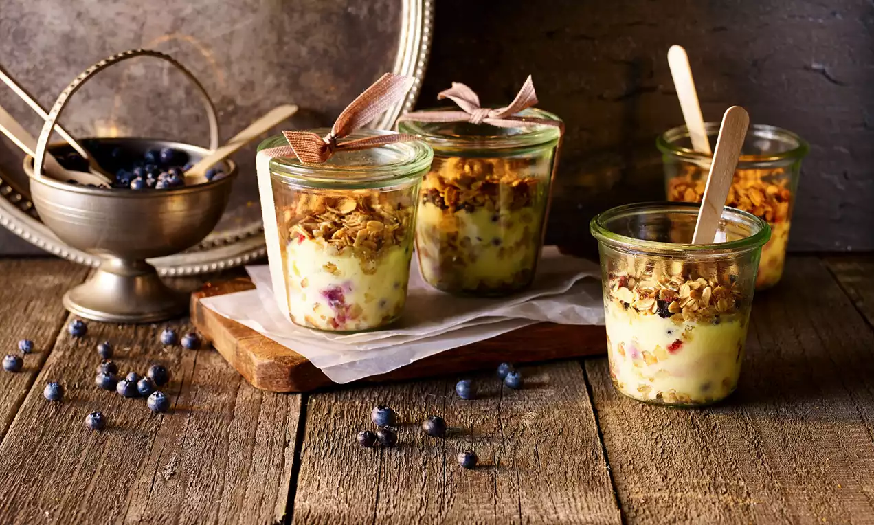 Cam kavanozlarda renkli lorlu karışım üzerine gevrek müsli tabakası, dekoratif kaşıklarla rustik ahşap zemin üzerine yerleştirilmiş