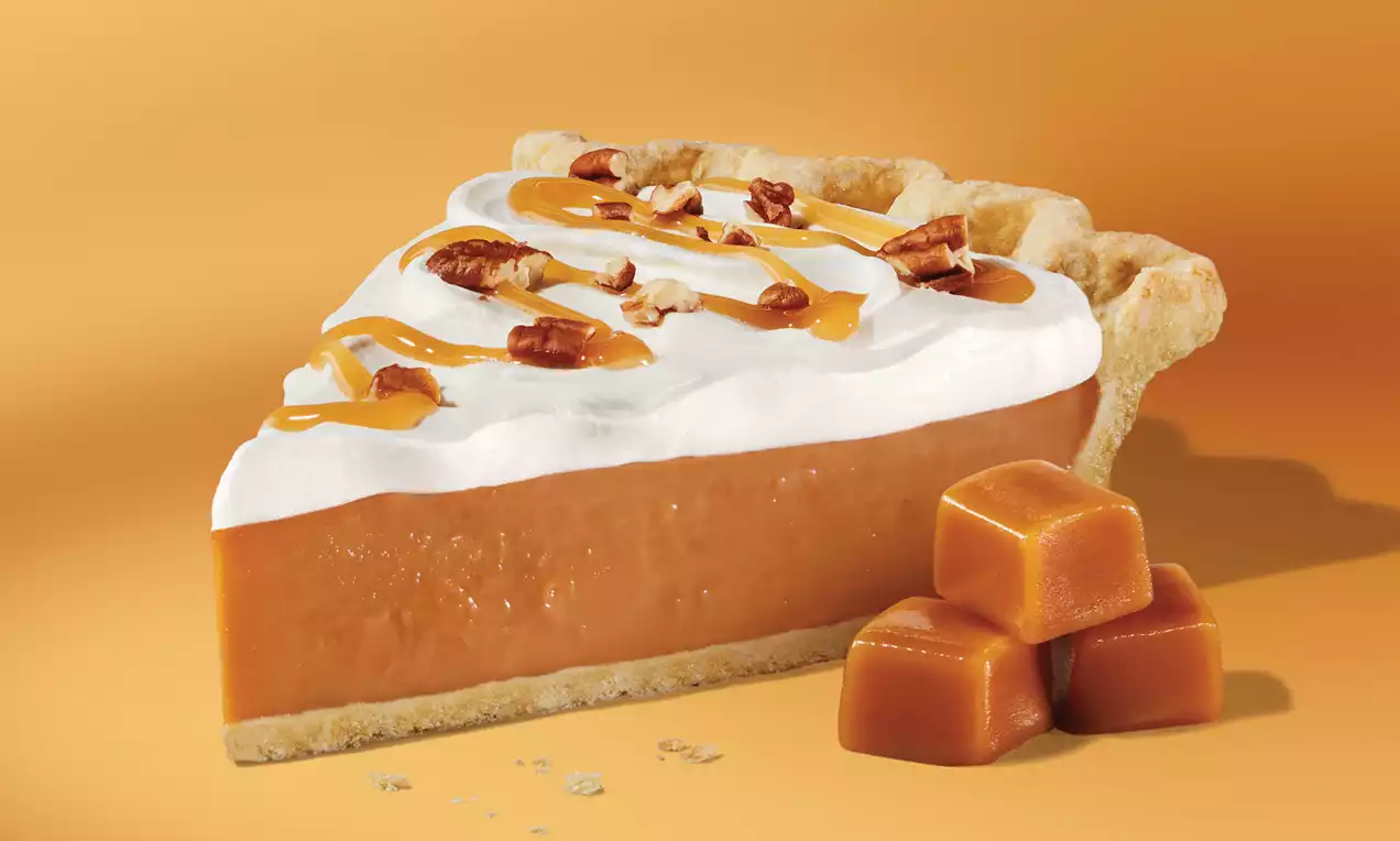 A slice of butterscotch pie with smooth caramel-colored filling, white whipped topping, pecan pieces, caramel drizzle, and a flaky crust