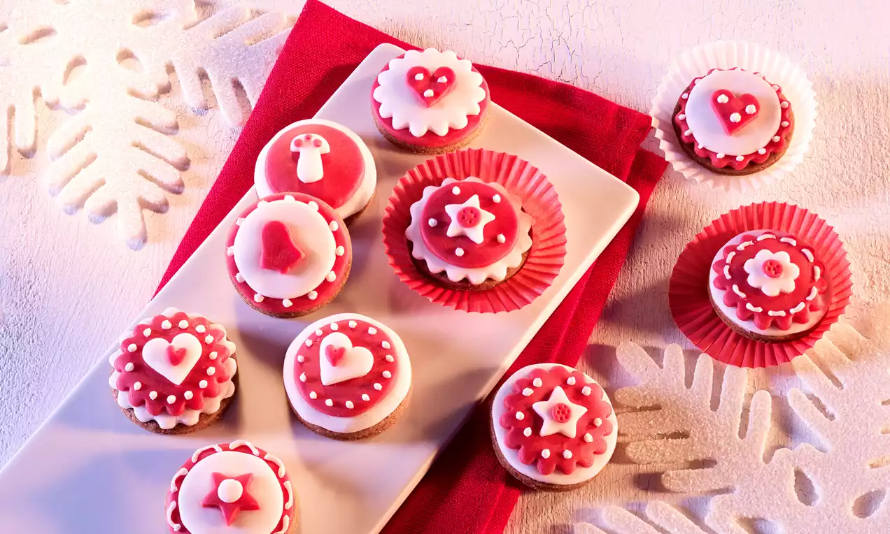 Petits biscuits ronds rouges et blancs décorés de motifs nordiques en sucre sur une assiette blanche posée sur une nappe rouge