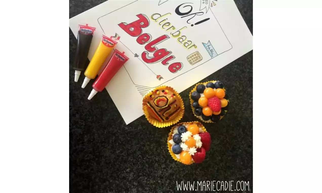 Cupcakes met kleurrijke decoratie van blauwe bessen, frambozen en oranje snoepdecoraties naast tubes glazuur op een donkere ondergrond