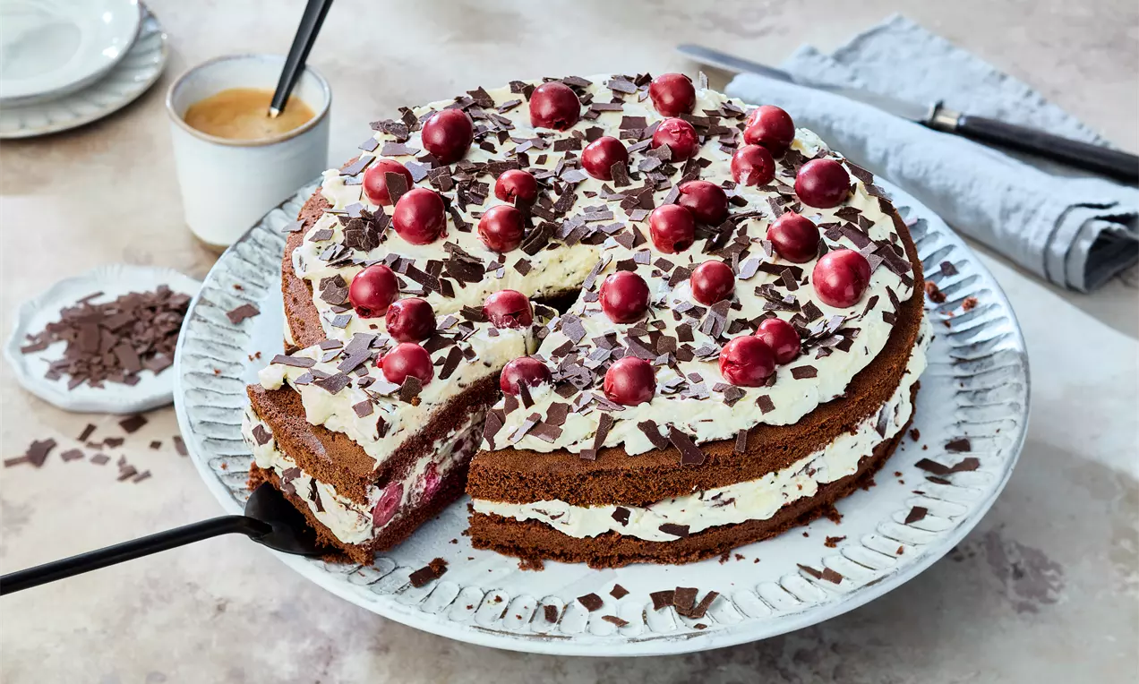 Stracciatella-Kirsch-Torte mit luftiger Biskuitbasis, cremiger Mascarponefüllung, fruchtigen Kirschen und dunklen Schokoraspeln – dekorativ angerichtet auf einer Tortenplatte