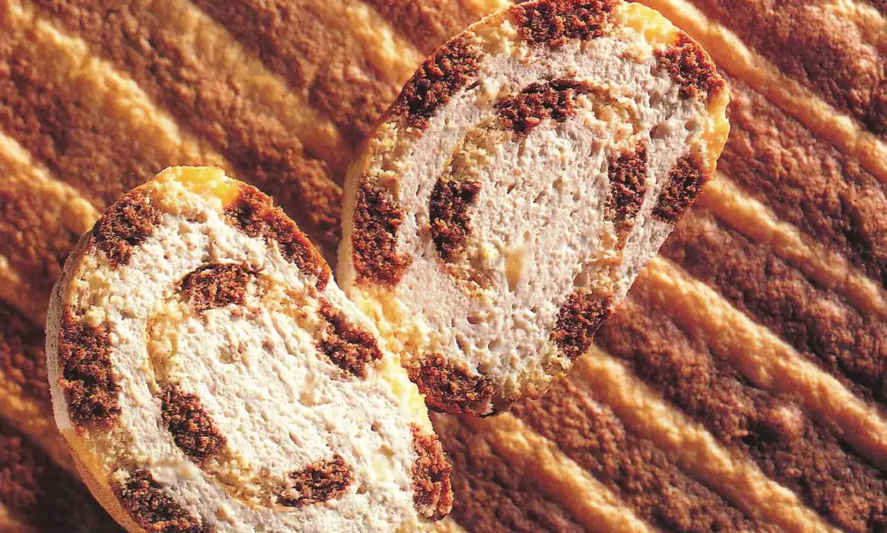 Luchtige bananenrol met spiraalpatroon van goudgele cake en bruine vulling, op een achtergrond van lagen goudbruine textuur