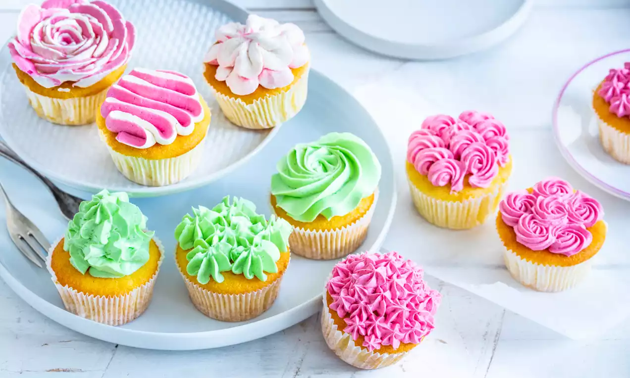 Cupcakes met kleurrige bloemenvormige toppings in roze, groen en wit, gepresenteerd op lichte borden tegen een witte achtergrond