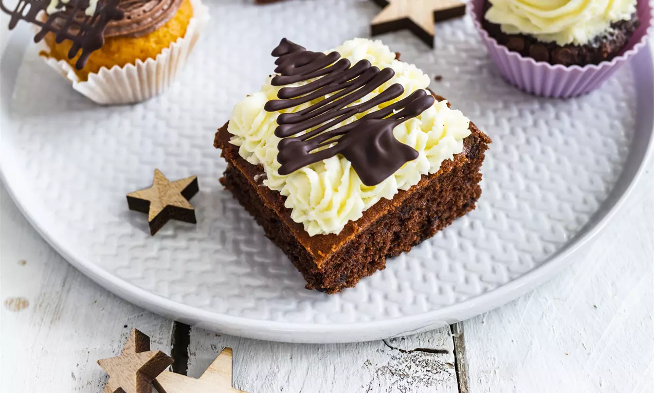 Шоколадово квадратно парче с пухкав бял крем, украсено с тънки линии тъмен шоколад, разположено сред дървени звездички върху светла чиния