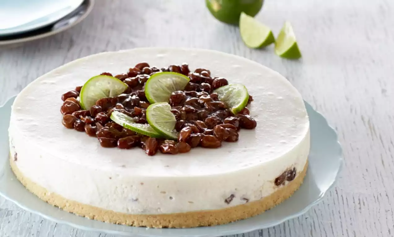 Ronde kwarktaart met romige witte vulling en rozijnen, gegarneerd met glanzende limoenpartjes op een lichtblauw schaalbord