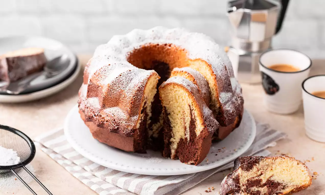 Marmorkuchen mit goldgelber und schokoladenbrauner Marmorierung, gestäubt mit Puderzucker auf weißem Teller mit Streifenserviette drapiert