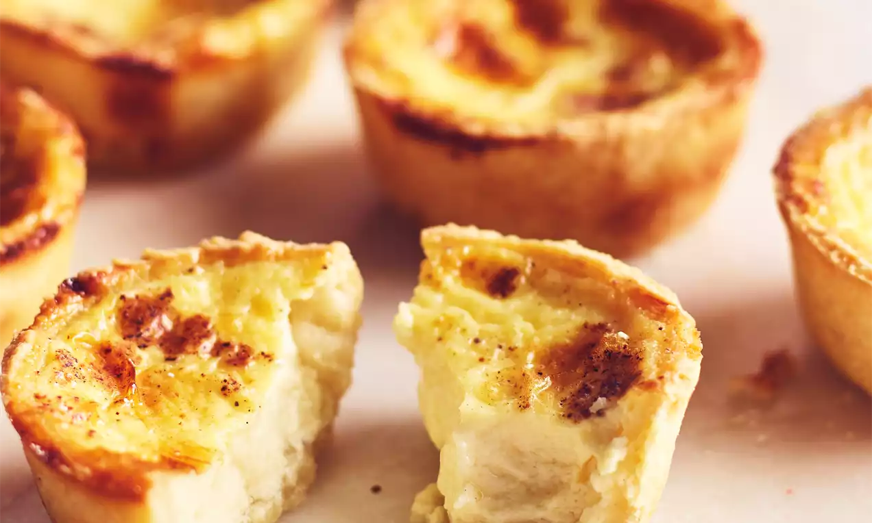 Golden egg tart with a flaky, lightly browned crust and creamy custard center, one halved to reveal its soft, smooth texture