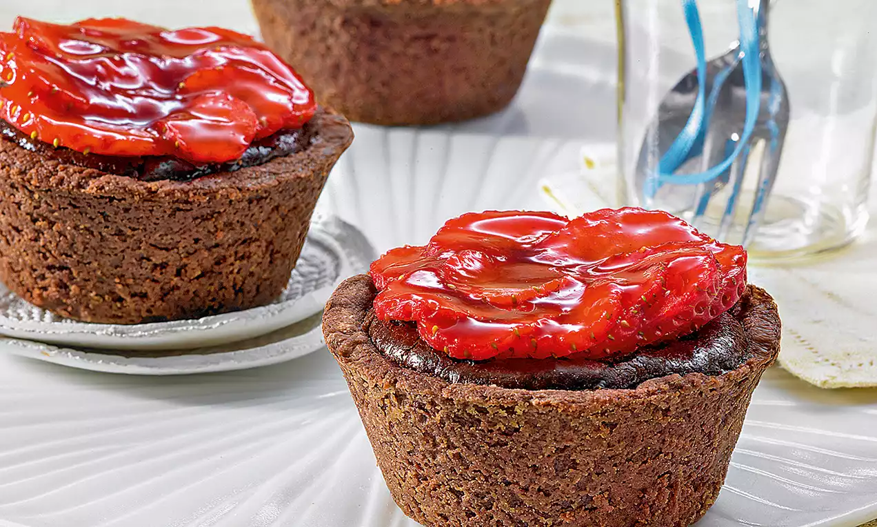 Muffin au chocolat brun foncé avec une surface lisse garni de fraises brillantes en tranches sur une assiette blanche texturée