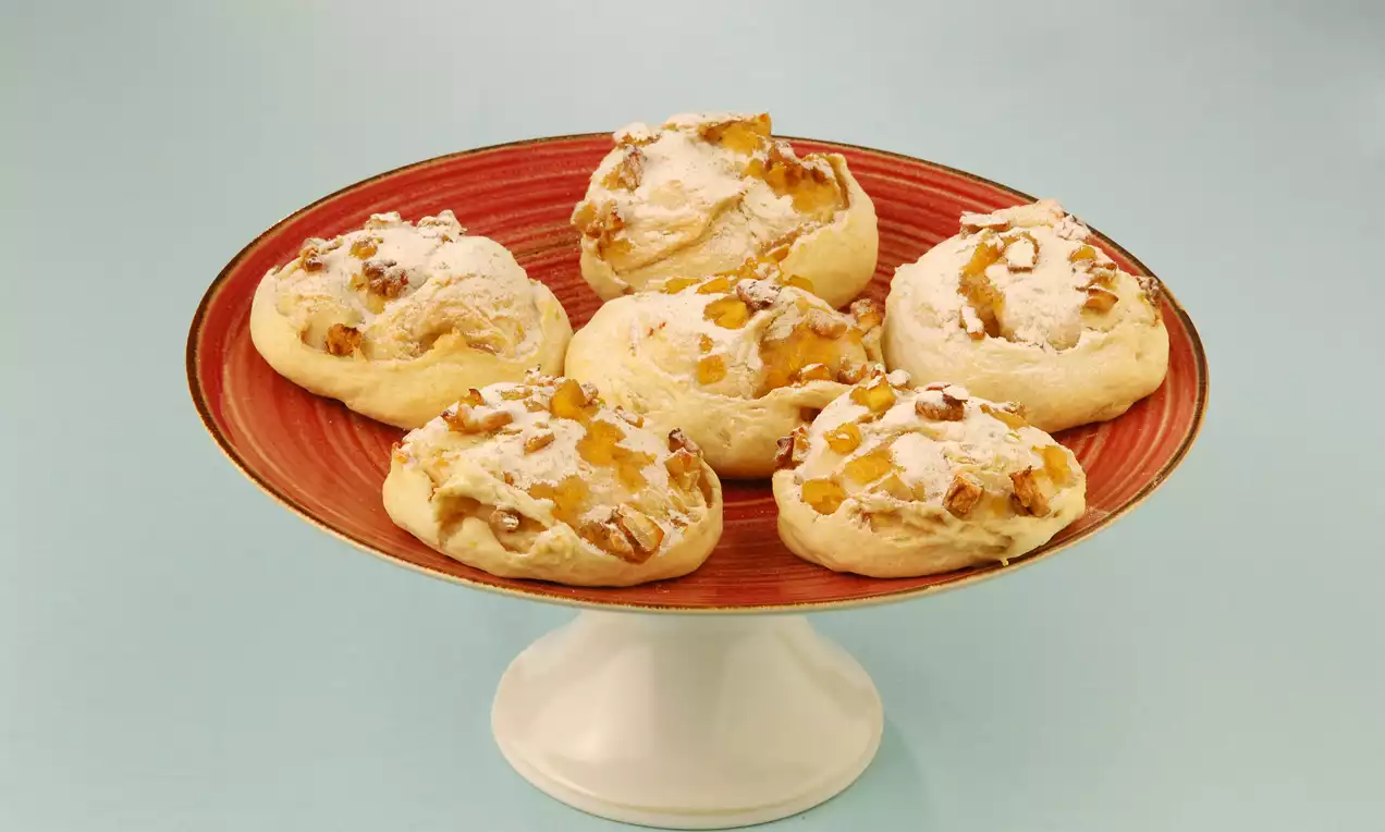 Altın sarısı elmalı puflar, kırmızı tabakta sergilenmiş, ince pudra şekeriyle süslenmiş ve hafif kabarık bir görünüme sahip