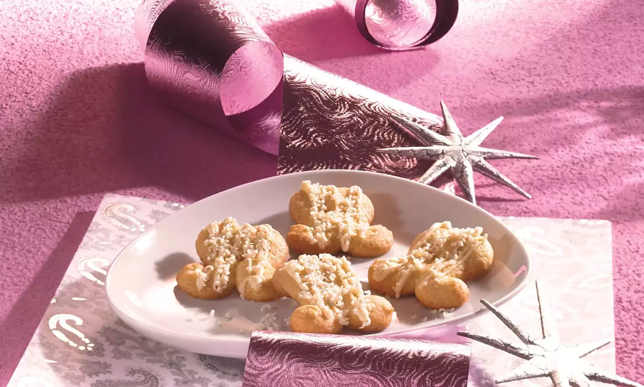 Kıvrımlı yıldız şekilli kurabiye, beyaz tabakta sergilenen, pudra şekeri detayları ve pembe metalik dekore edilmiş bir arka planla süslenmiş