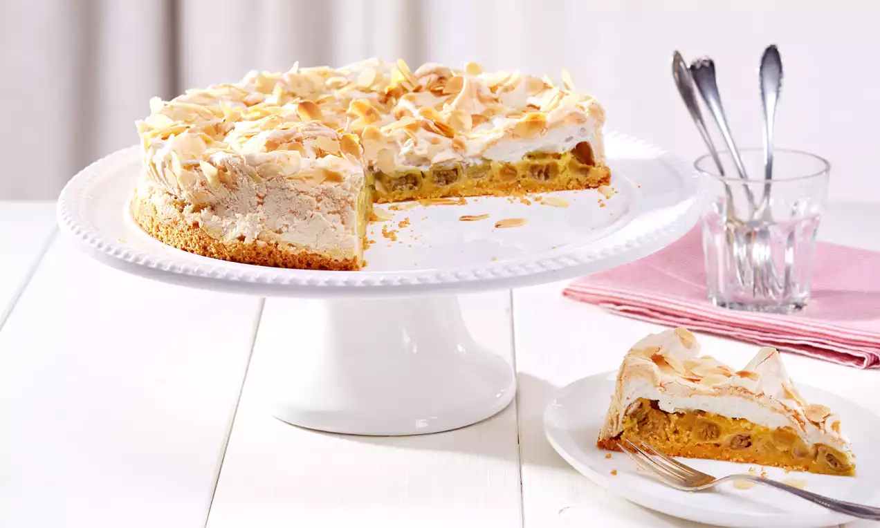 Schneekuchen mit goldbraunem Boden, weißer Baiserhaube und Stachelbeeren, dekoriert mit Mandelsplittern, auf weißer Tortenplatte