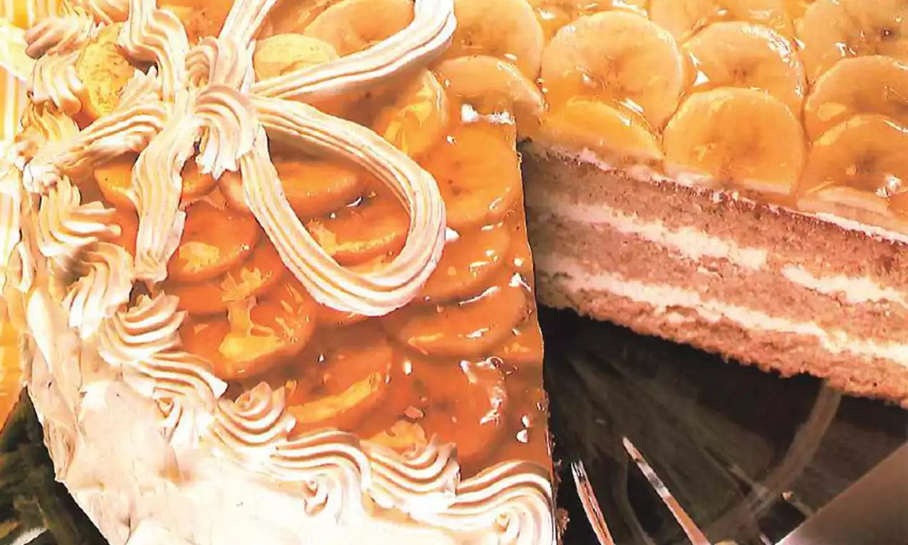 Gâteau à étages avec crème légère, tranches de banane dorées sous un nappage brillant et bord décoré de volutes de chantilly