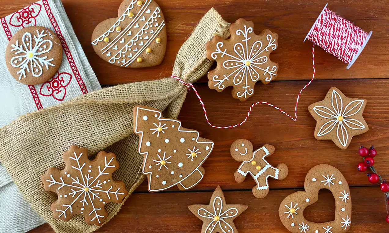 Lebkuchen in verschiedenen Formen mit filigranem weißem Zuckerguss dekoriert, auf Holztisch mit Sackleinen und roter Schnur arrangiert