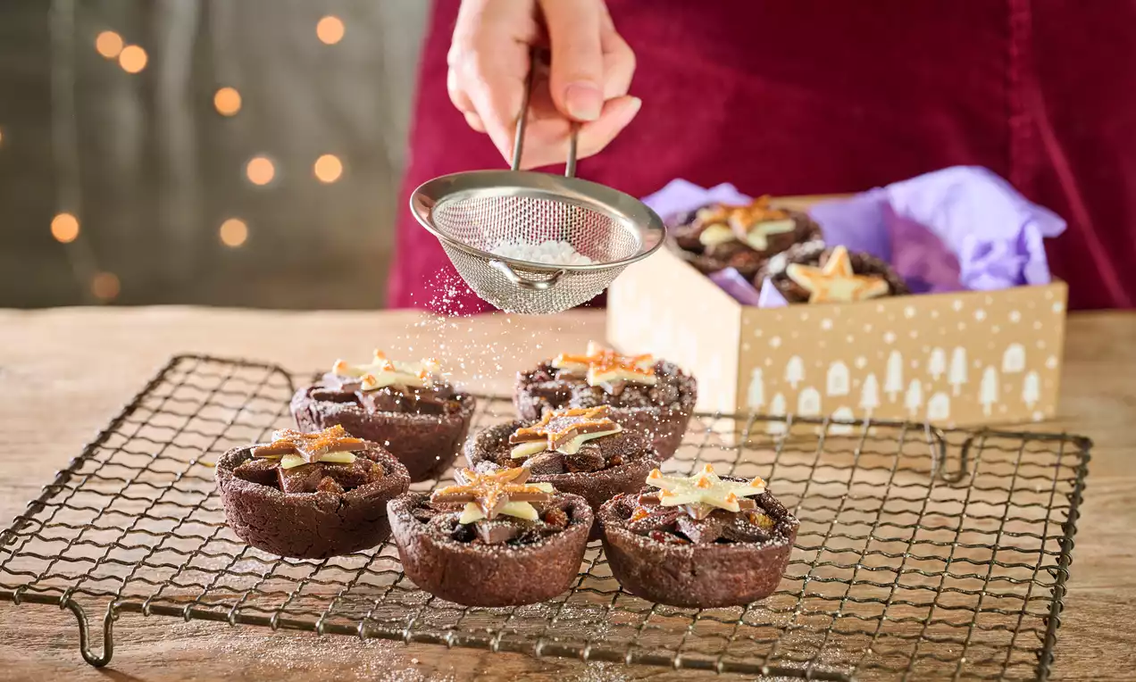 Chocolate mince pies with deep brown crusts, filled with rich filling, topped with golden slivers and dusted with powdered sugar