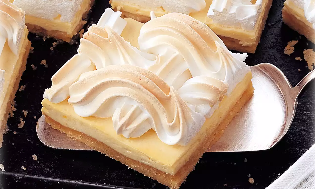 Carré de tarte avec une base dorée, crème jaune pâle et généreux tourbillons de meringue dorée sur une pelle métallique