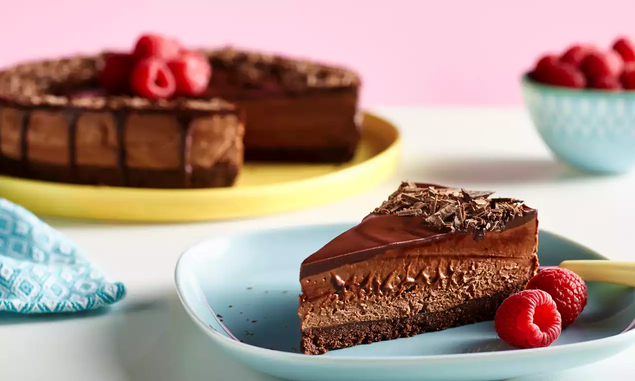 No Bake Chocolate Cheesecake med lag av mørk sjokolade på sprø bunn, dekorert med sjokoladespon og bringebær på lys blå tallerken