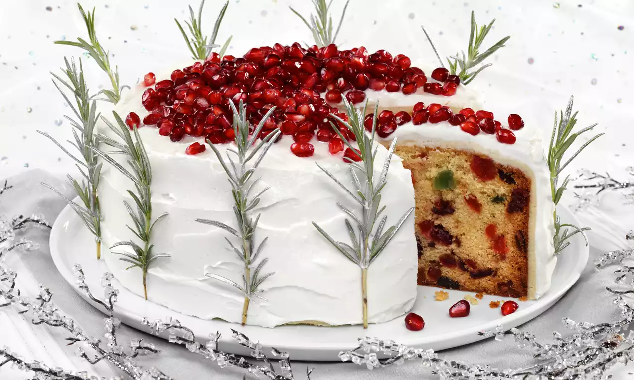 Snow Queen Christmas cake with smooth white icing, ruby red pomegranate seeds, rosemary sprigs and a colorful fruit interior