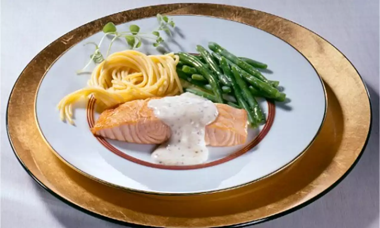 Zartrosa Lachsfilet mit hellcremiger Sauce, daneben grüne Bohnen und blassgelbe Spaghetti auf einem weißen Teller mit Goldrand angeordnet
