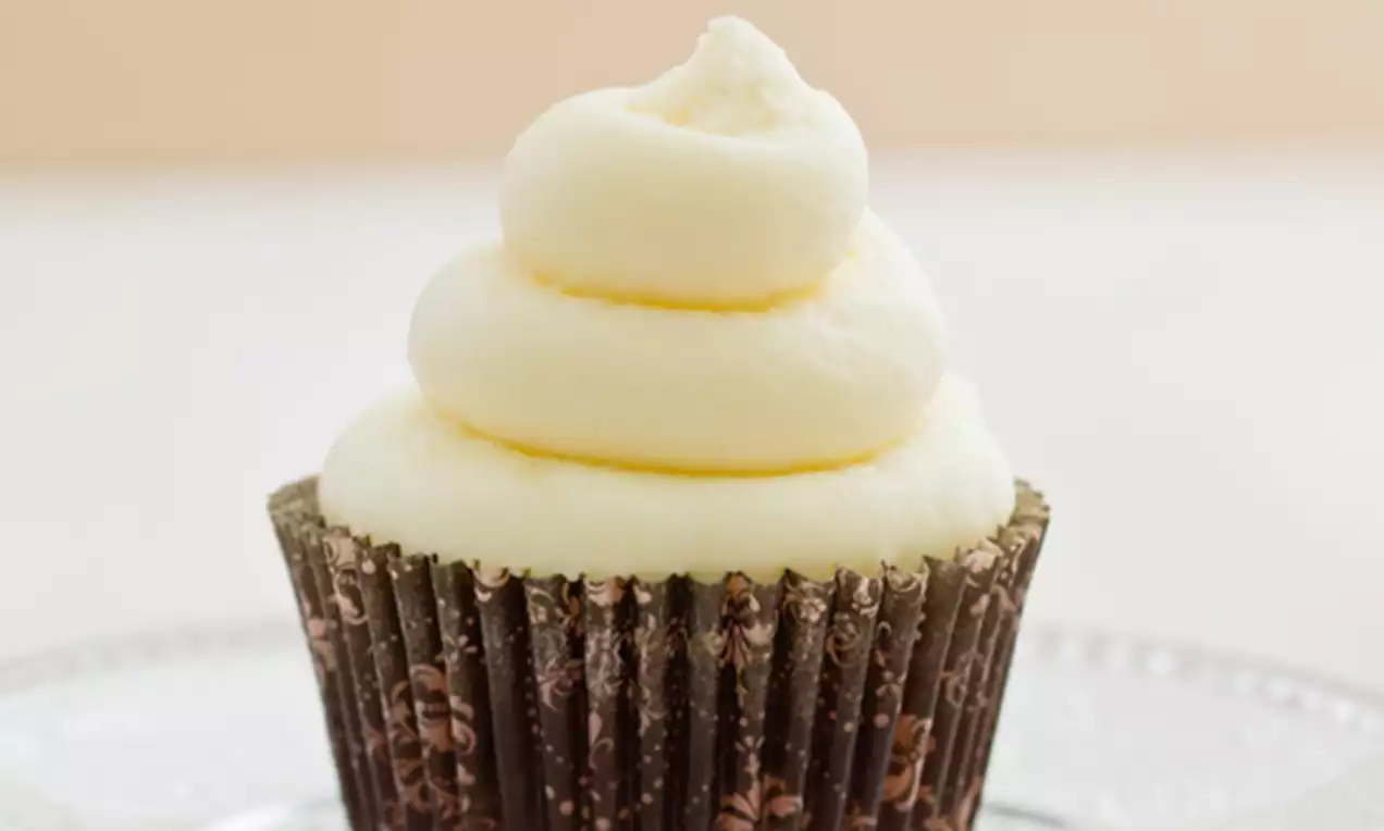 Cupcake con base oscura decorada con motivos florales y crema de yogur fresca en espirales suaves color blanco marfil sobre plato transparente