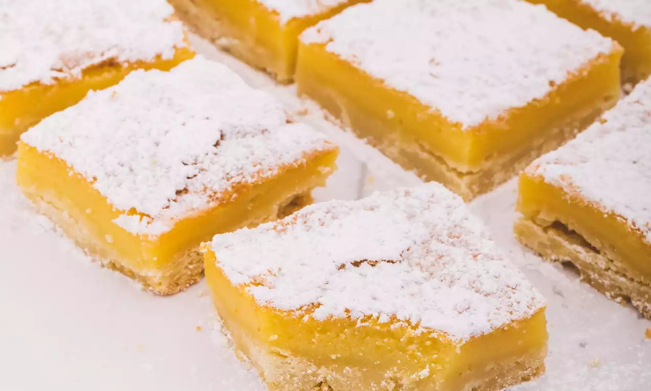 Bocados cuadrados con relleno naranja brillante y capa superior espolvoreada con azúcar glas sobre base dorada dispuestos en papel blanco