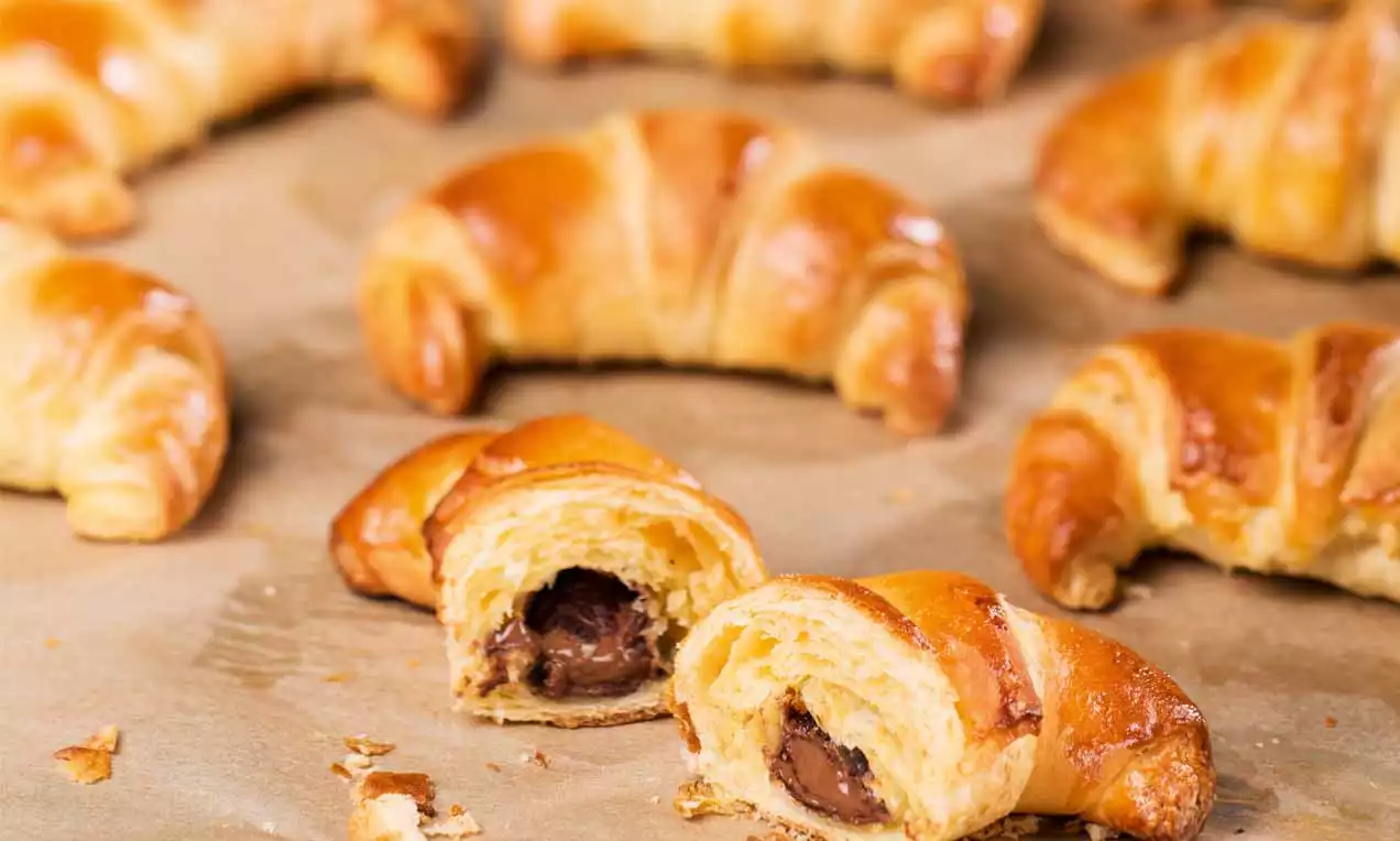 Čokoladni kroasani zlatnosmeđe, sjajne korice, prozračne unutrašnjosti s punjenjem od tamne čokolade, položeni na papir za pečenje