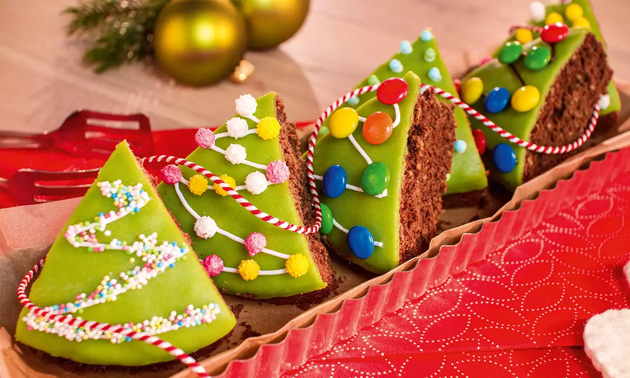 Dolci triangolari di pan di spagna al cioccolato con glassa verde brillante, decorati con caramelle colorate e zucchero su un vassoio festivo