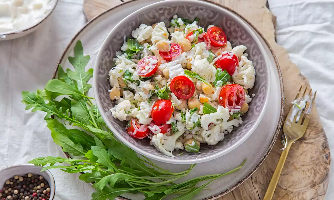 Vibrant chickpea salad with creamy cauliflower, juicy cherry tomatoes, fresh parsley and arugula on a patterned bowl and wooden board