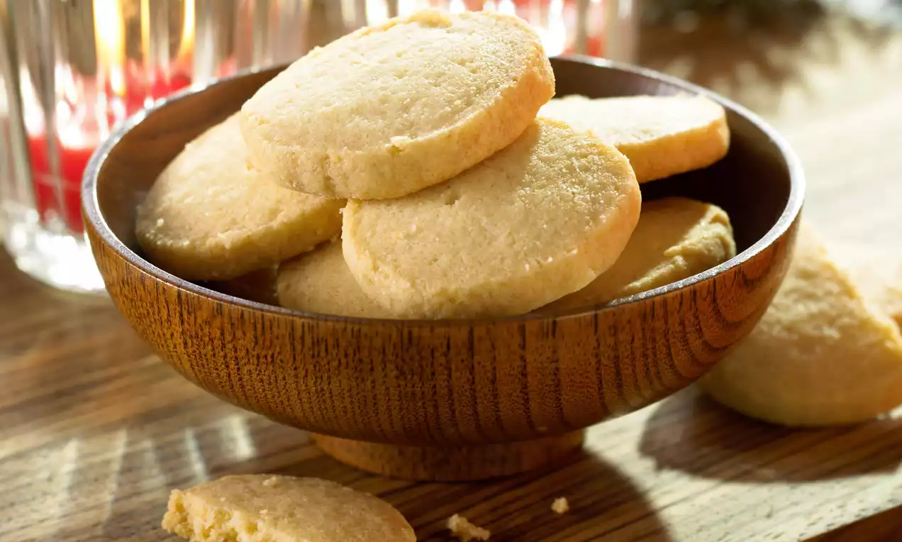 Goudgele maiskoekjes met een licht korrelige textuur, rond en plat, nonchalant gestapeld in een houten kom op een houten tafel