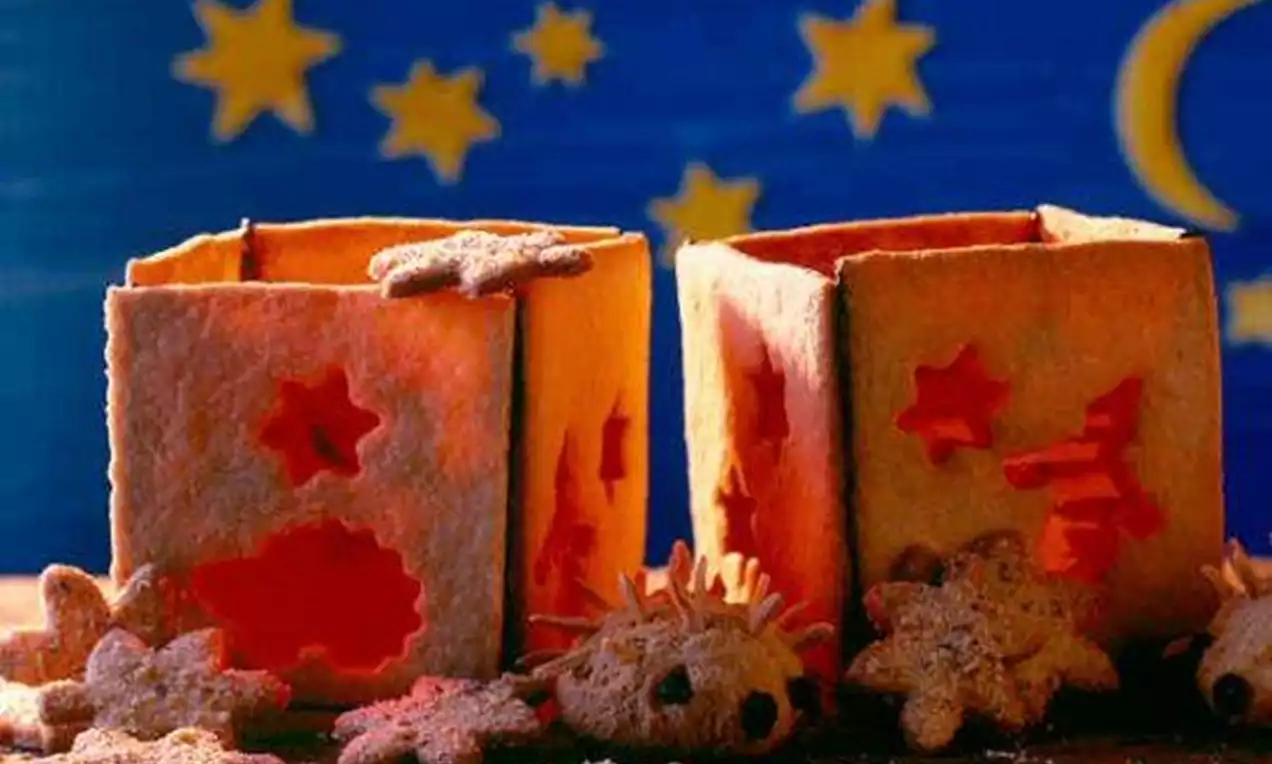 Deux lanternes carrées faites de pâte dorée avec des découpes en forme d'étoiles, entourées de biscuits en étoile sur fond étoilé bleu