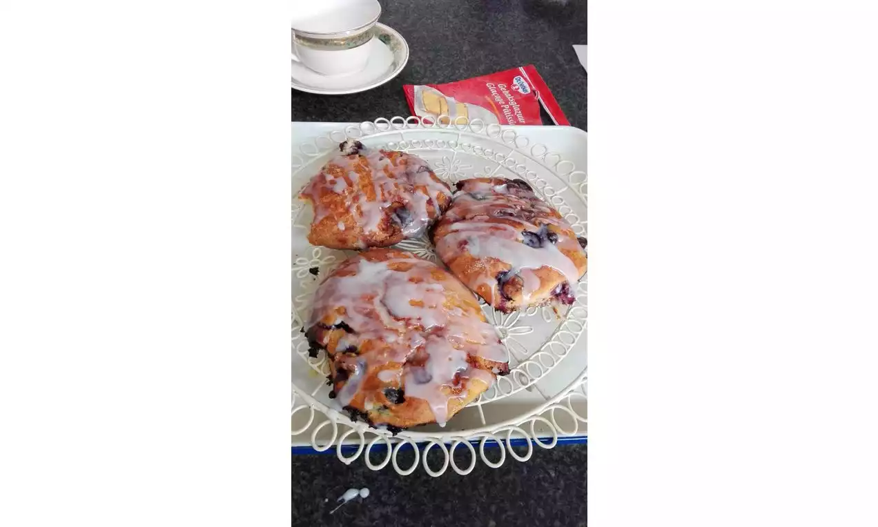 Glanzende glazuurdriehoeken met blauwe besvlekken, lichtbruin en zacht, op een sierlijk wit bord tegen een donkere ondergrond