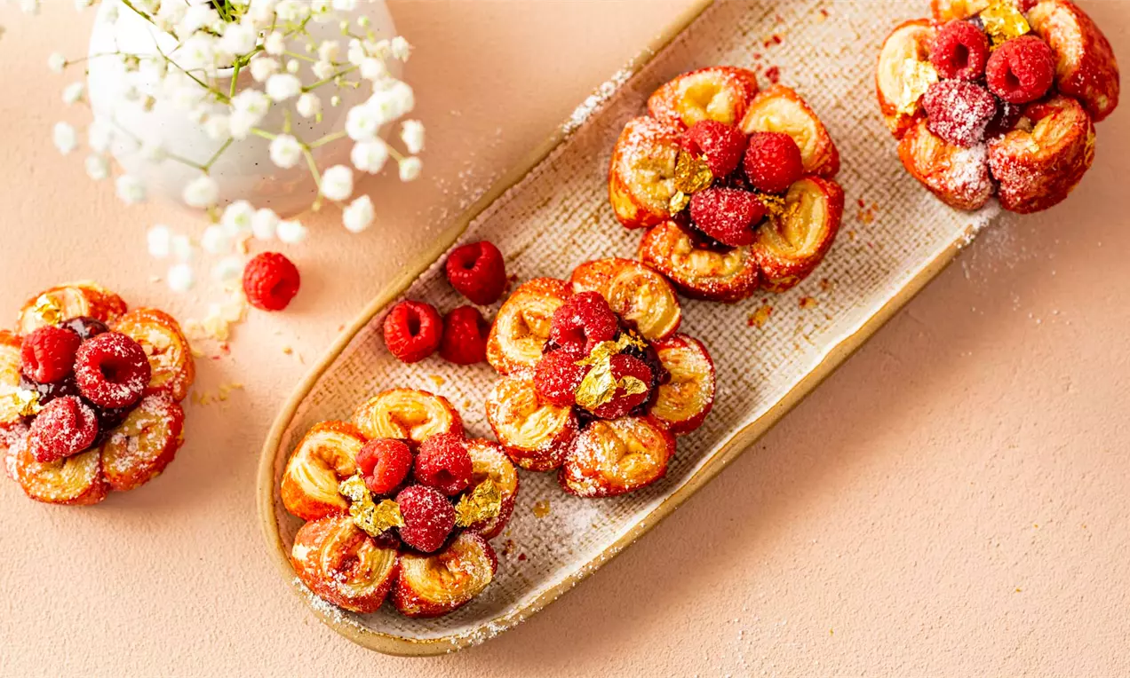 Златисто кафяви бутер цветя с хрупкави листенца, гарнирани с малини и поръсени с пудра захар, подредени върху продълговата чиния