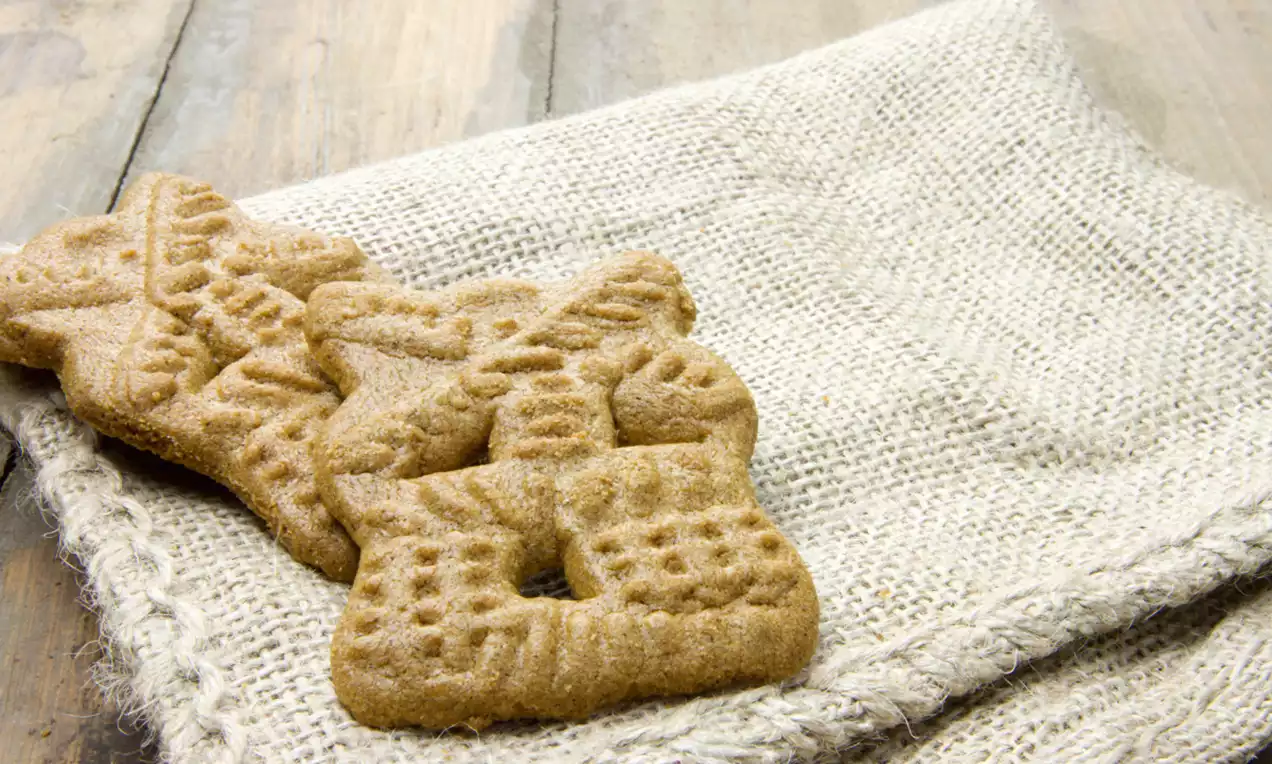Bruine speculaasjes met uitgesneden molenmotief, knapperig van textuur, liggend op een beige jute doek op een houten ondergrond